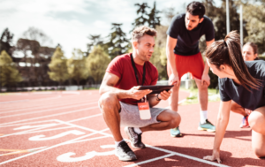 A coach kneels on a track to speak to three athletes