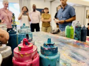 Messy bottles of paint in the foreground, with blurry members of the ISD team in the background.