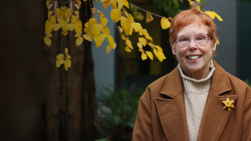 Dr. Nora Disis, standing outside with bright yellow fall foliage in the background.