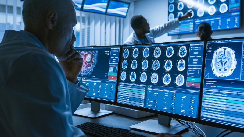 A researchers studies brain scan images on three computer monitors